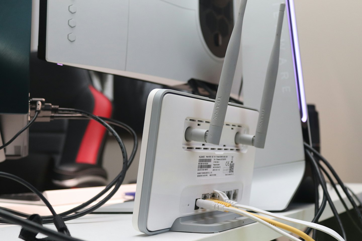 White and grey router with antennas and ethernet cables on desk.