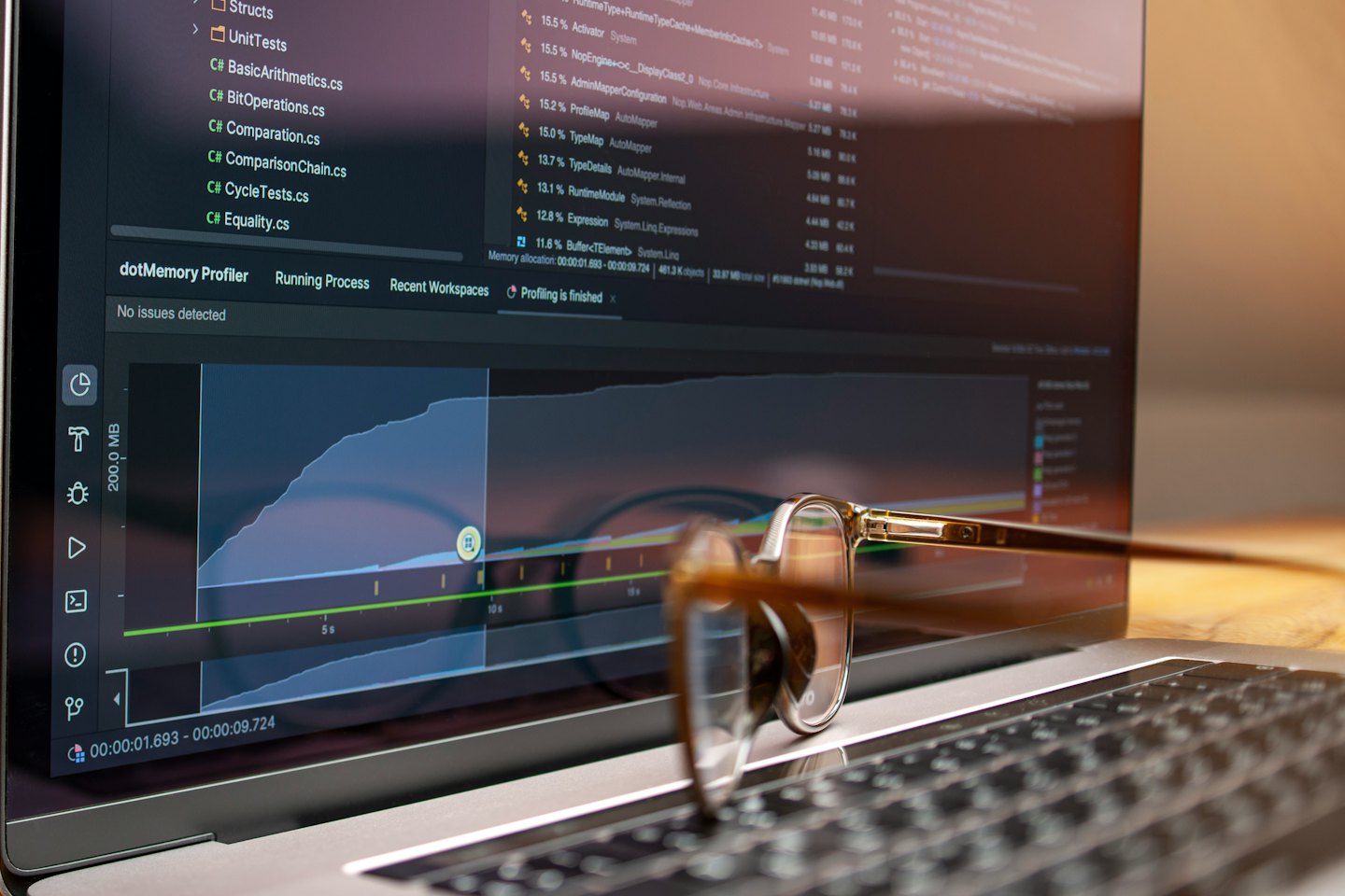 Laptop screen shows code and a memory profiler graph with eyeglasses on the keyboard.